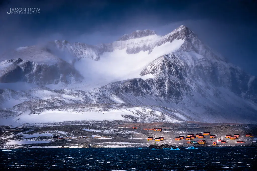 A stormy mountainous scene at the tip of the Antarctic peninsular. An Antarctic research base is seen at the foot of the mountain