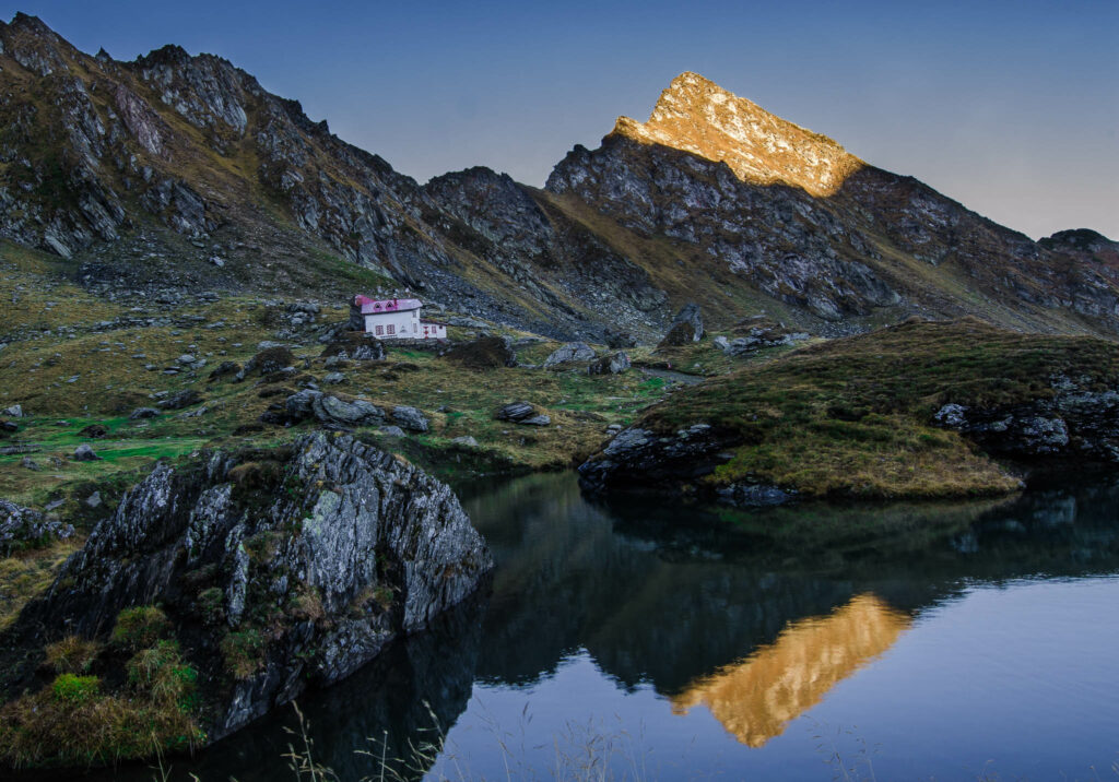 The dramtic landscape at the top of the Transfagarasan Pass in Romania. A lake is overshadowed by mountain peaks. The sun just casting its light on the top of the peaks