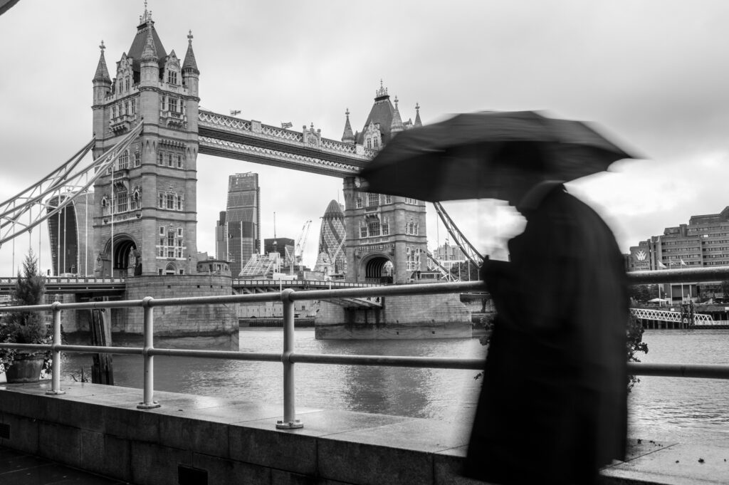 Rainy scene in London as man walks with umbrella with Tower Bridge in the background 