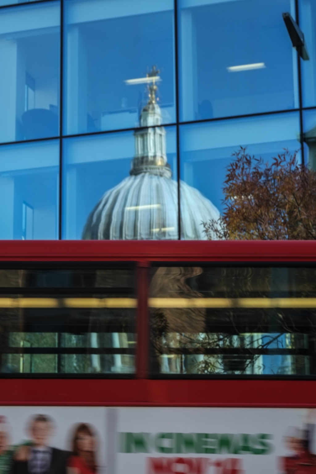 Red London bus passes reflection of St Pauls in modern office block.