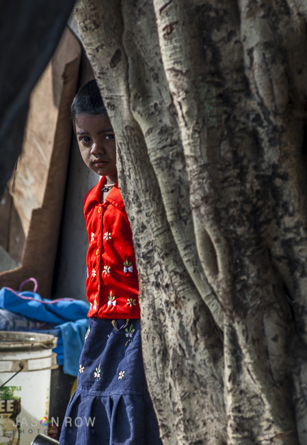 Young child peeks out from a slum beside a road in Mumbai