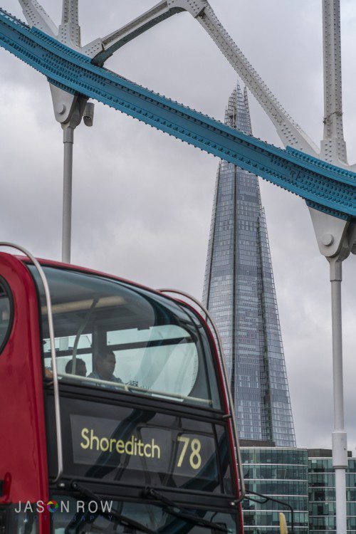 A red bus crosses Tower Bridge with the Shard London in the background