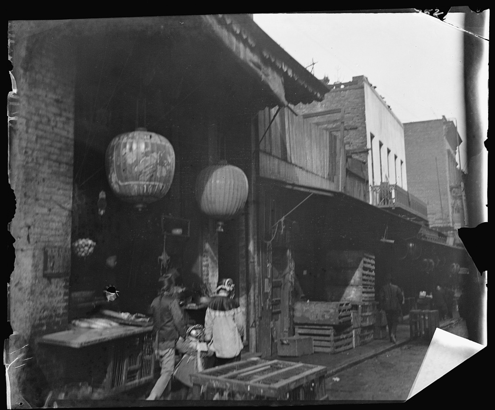 Two women and a child walking down a sidewalk between crates, Chinatown, San Francisco