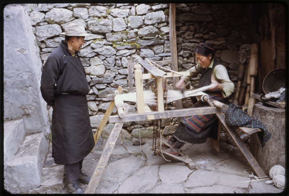 Photograph shows woman weaving on loom outdoors as a man watches, Lachung, Sikkim