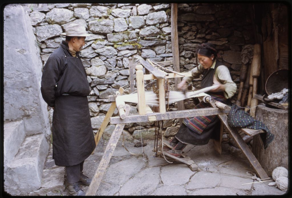 Photograph shows woman weaving on loom outdoors as a man watches, Lachung, Sikkim