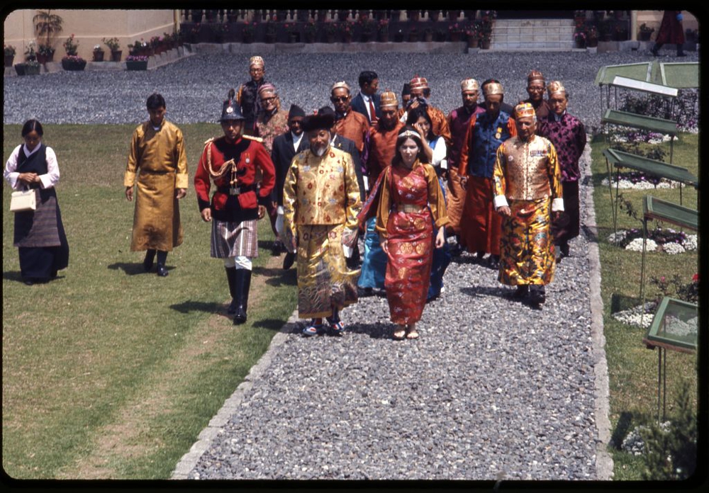 Photograph shows Palden Thondup Namgyal, King of Sikkim, and Hope Cooke, Queen of Sikkim, in brocaded dress, walking to the Tsuklakhang Main Temple (Palace Temple) for the King's birthday celebration, Gangtok, Sikkim.