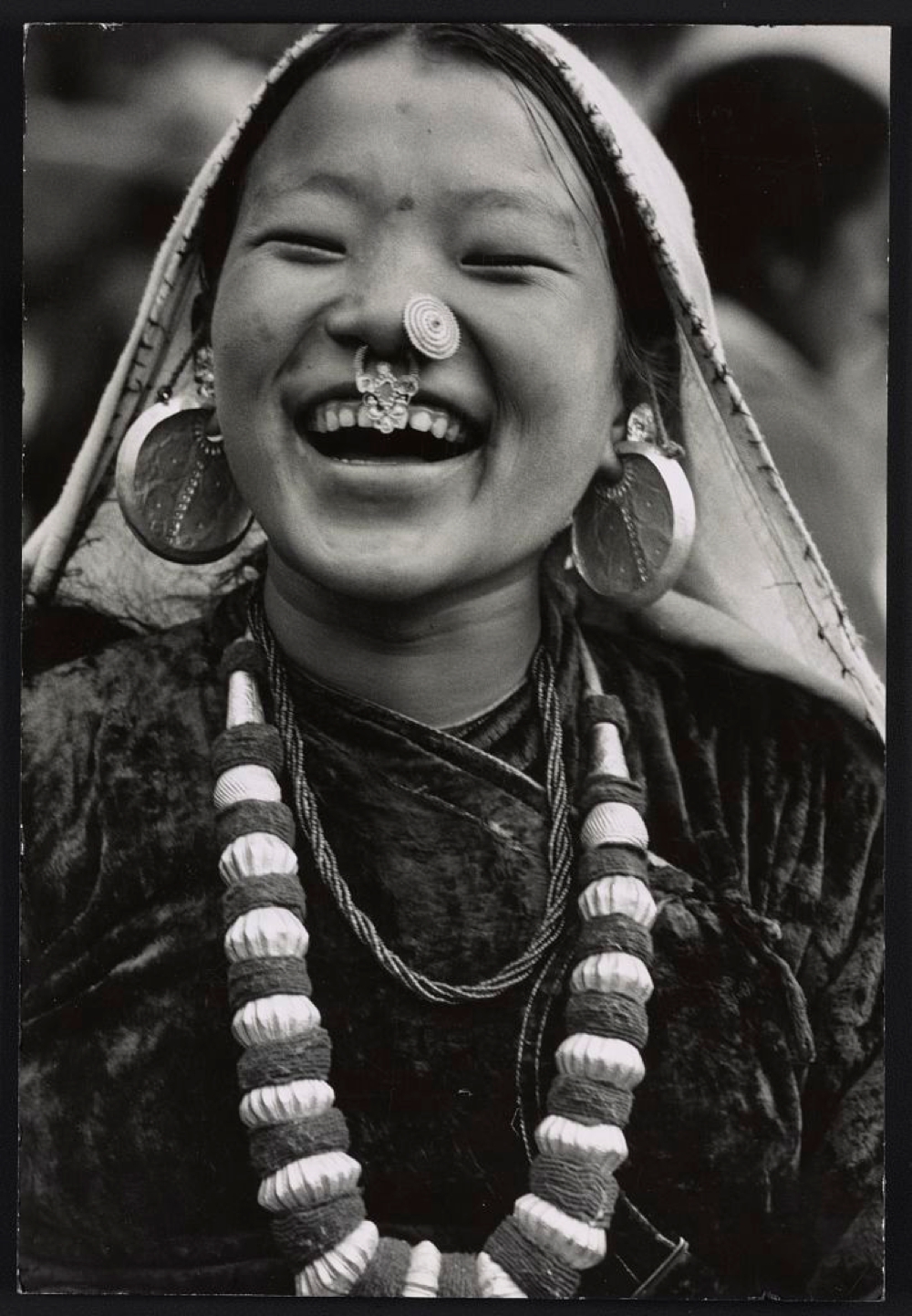 Photograph shows a Nepalese girl, head-and-shoulders portrait, facing front, smiling, wearing necklace, earrings and nose ornaments, in Sikkim.