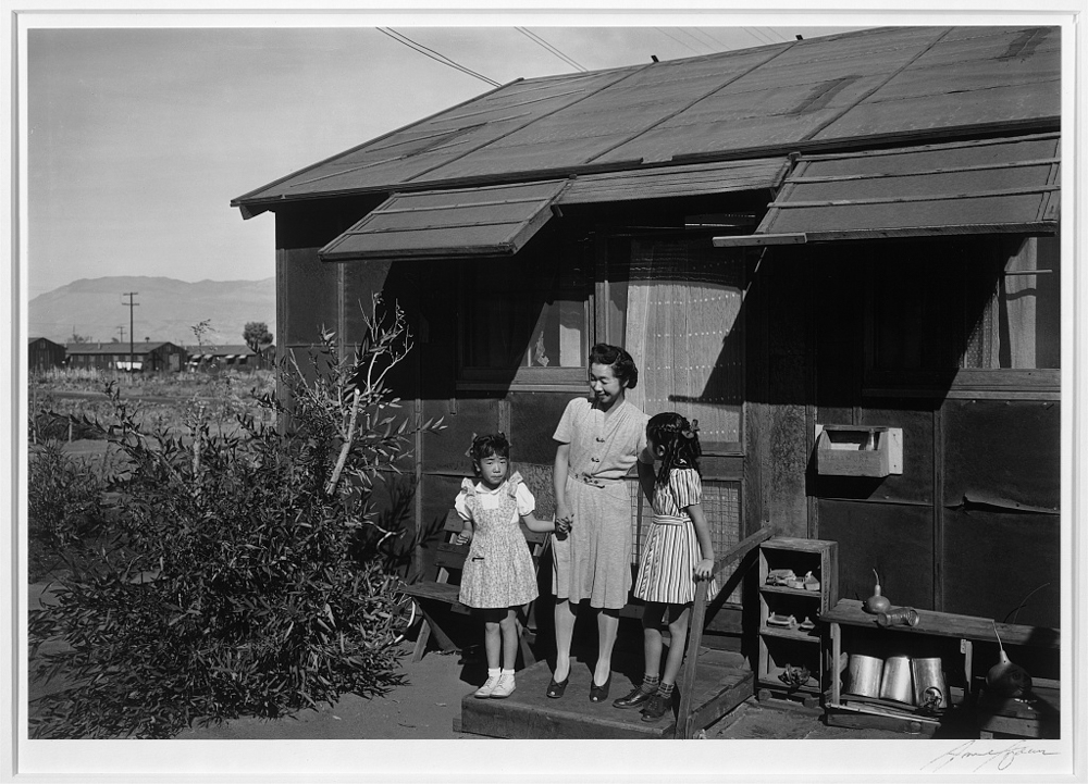 [Mrs. Yaeko Nakamura and her two children, Joyce Yuki (right) and Louise Tami (left), standing on the step at the entrance of a dwelling, Manzanar Relocation Center]