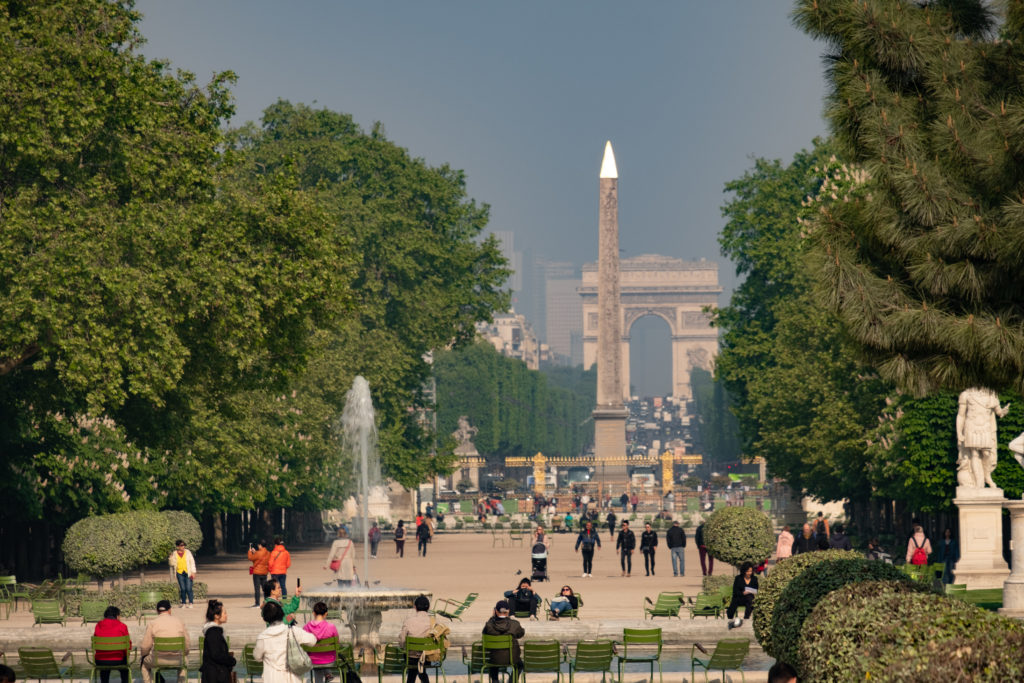 Static long shot looking through Tuileries Garden in Paris in springtime. The Luxor Obelisk and Arc De Triomphe are in the background