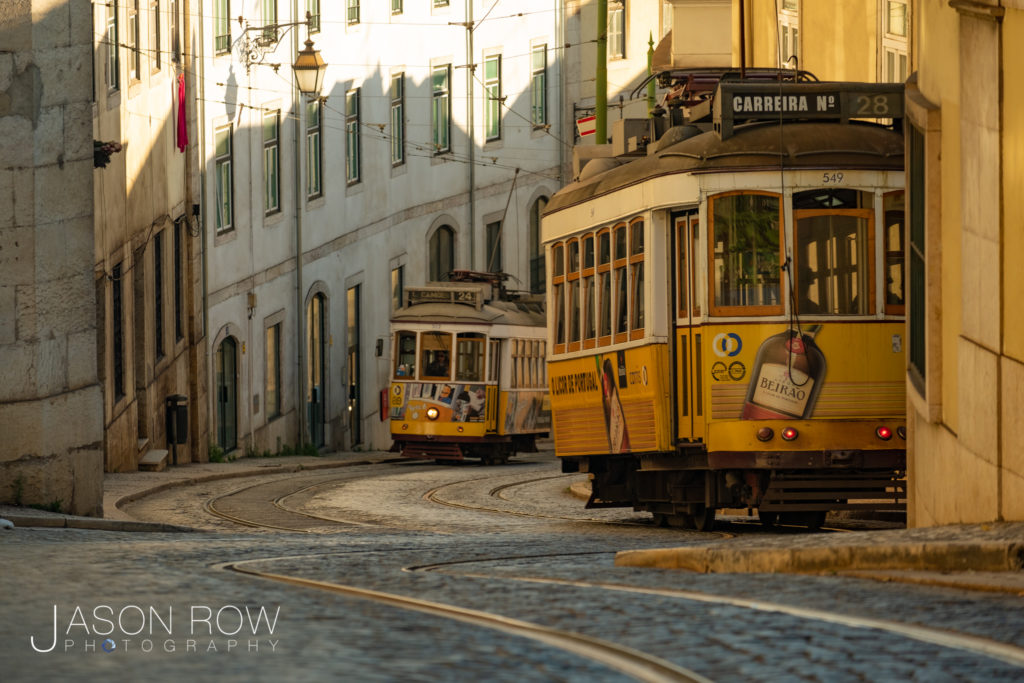 Telephoto clip of yellow old style tram line 28 climbing a hill in Lisbon, Portugal at dawn