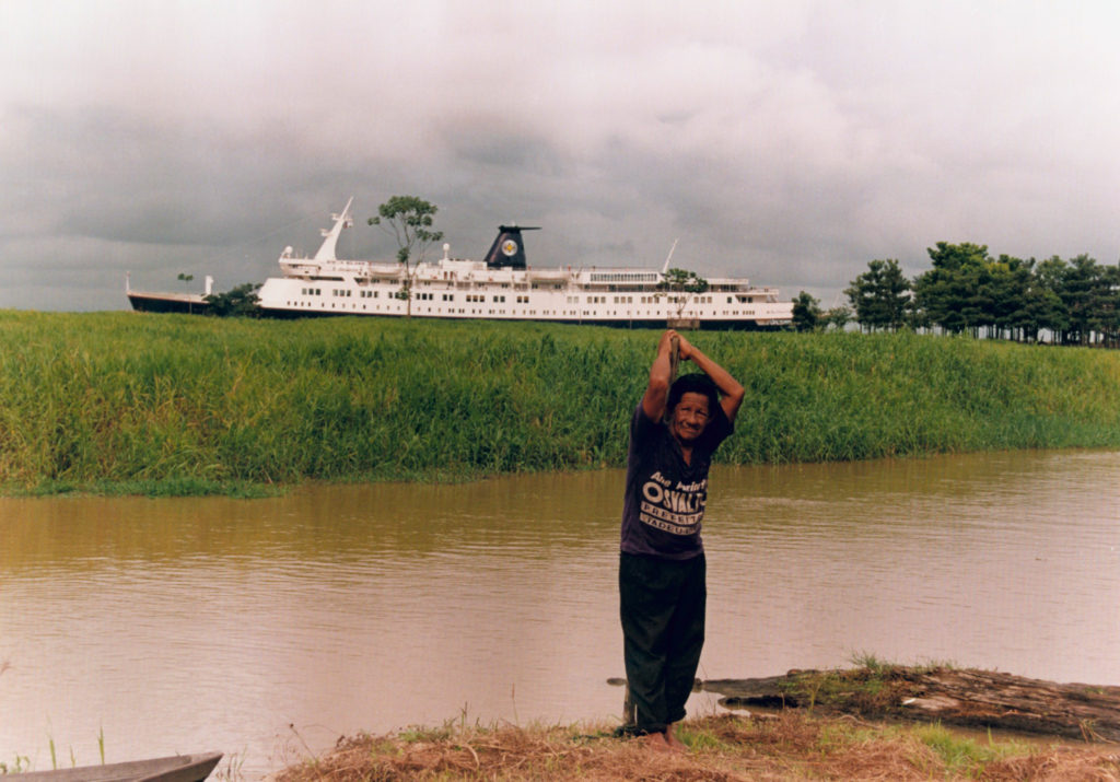 Amazonian man stands by Amazon river with ship in background 