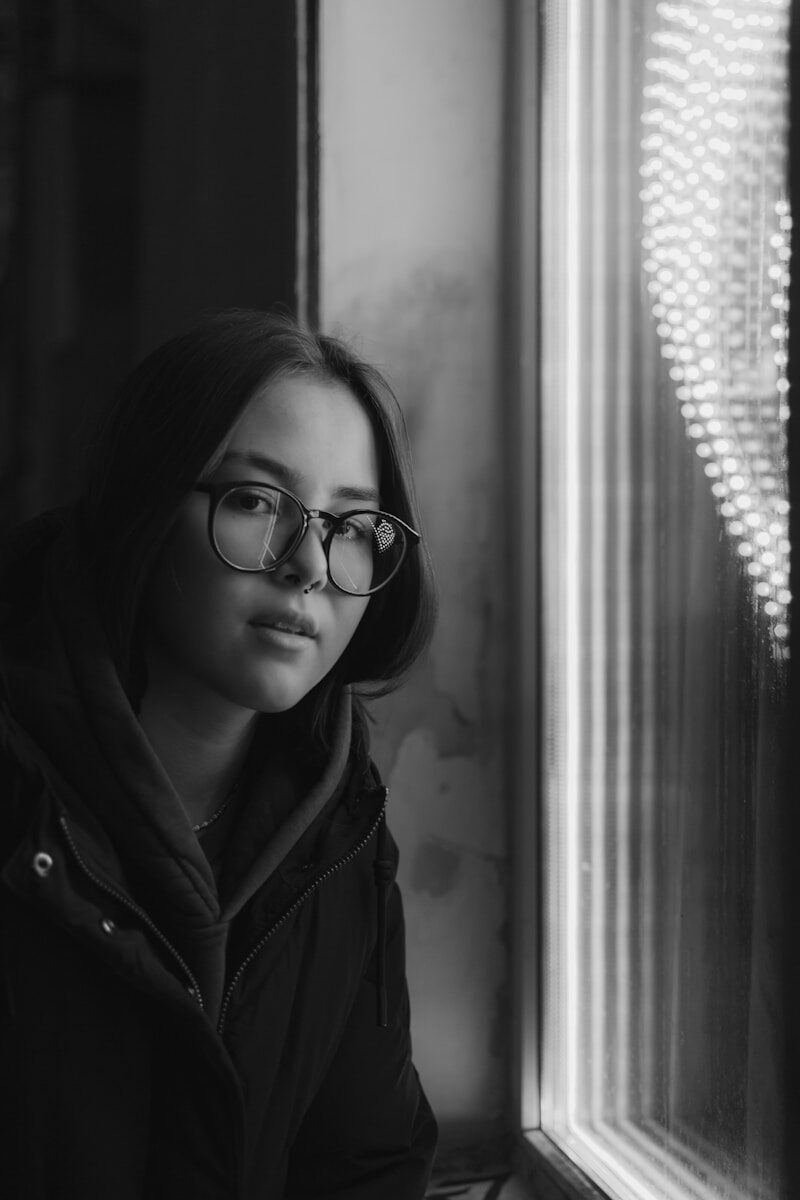 a black and white photo of a woman looking out a window