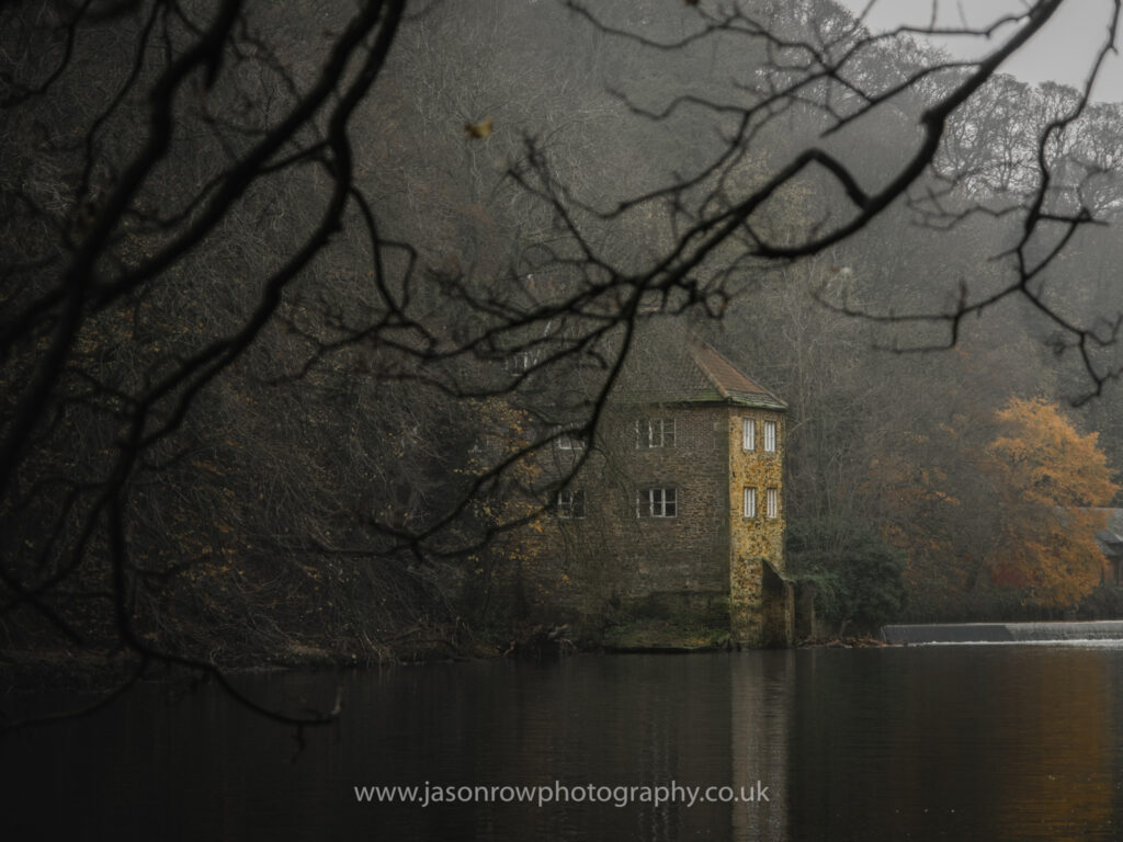 A misty derelict mill on the River Wear framed by bare branches