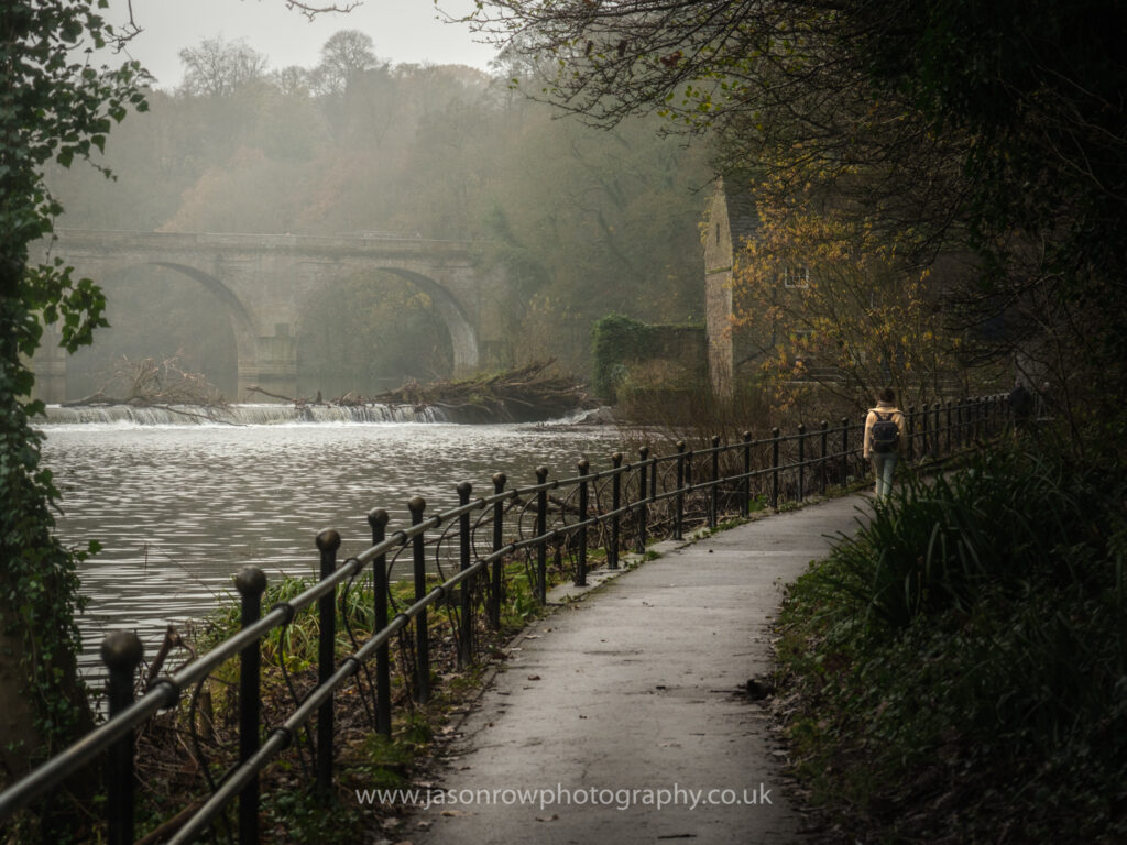A wintery scene from the riverside walk in Durham as a young woman walks into the distance 