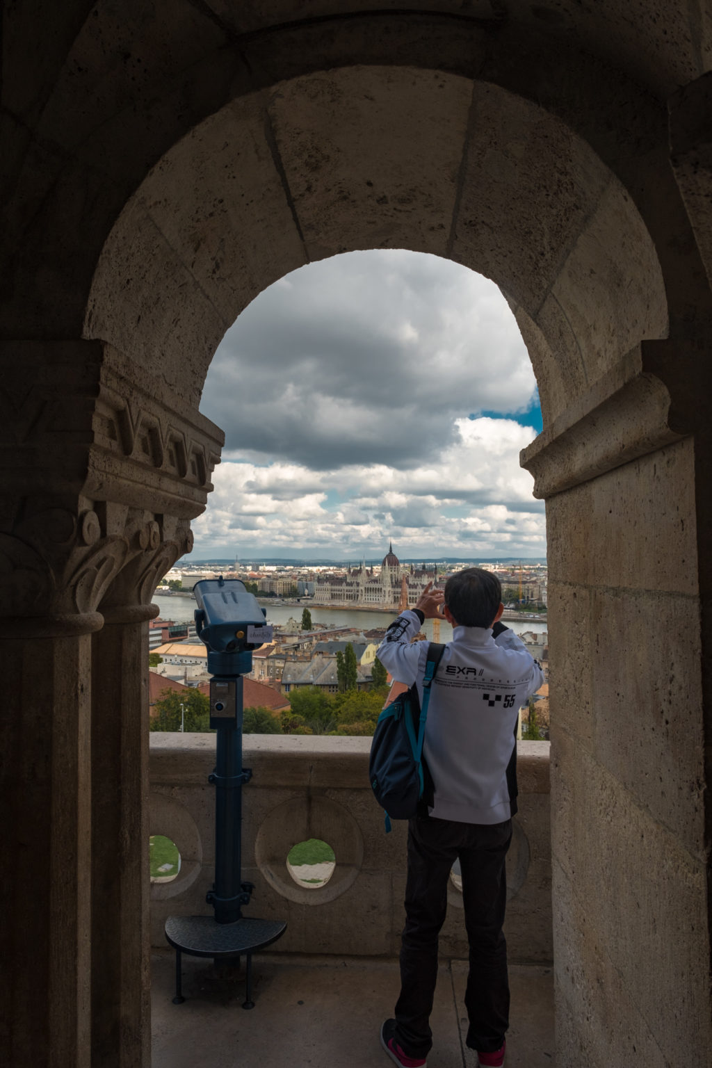 ourist takes photo of Budapest Parliament as seen through arch in Matthias Church, Hungary.