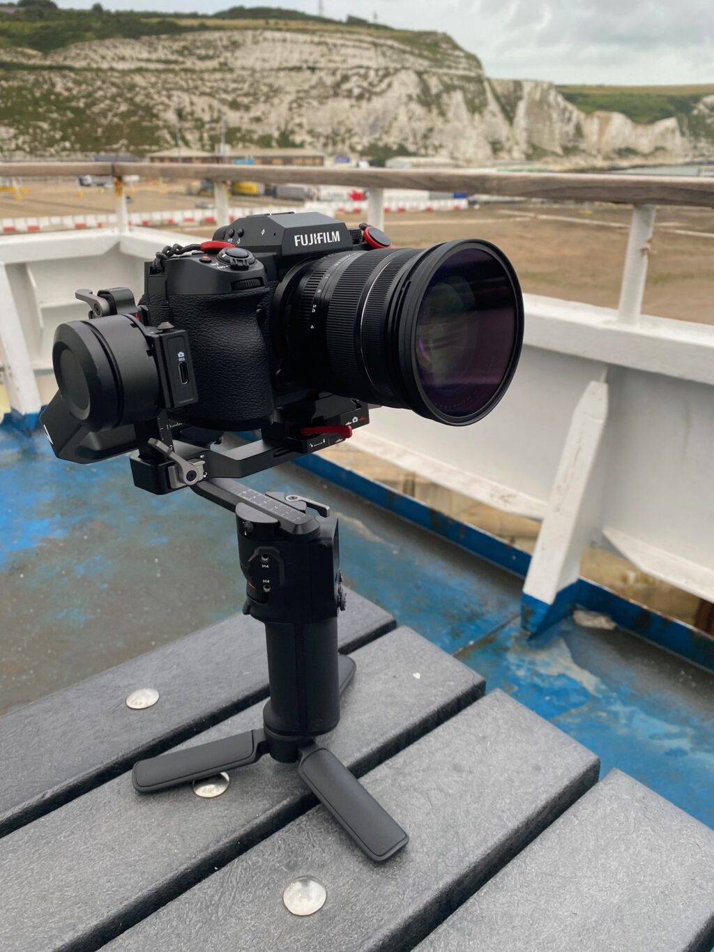 A Fujifilm camera on a DJI gimbal standing on a benchaboard a ferry