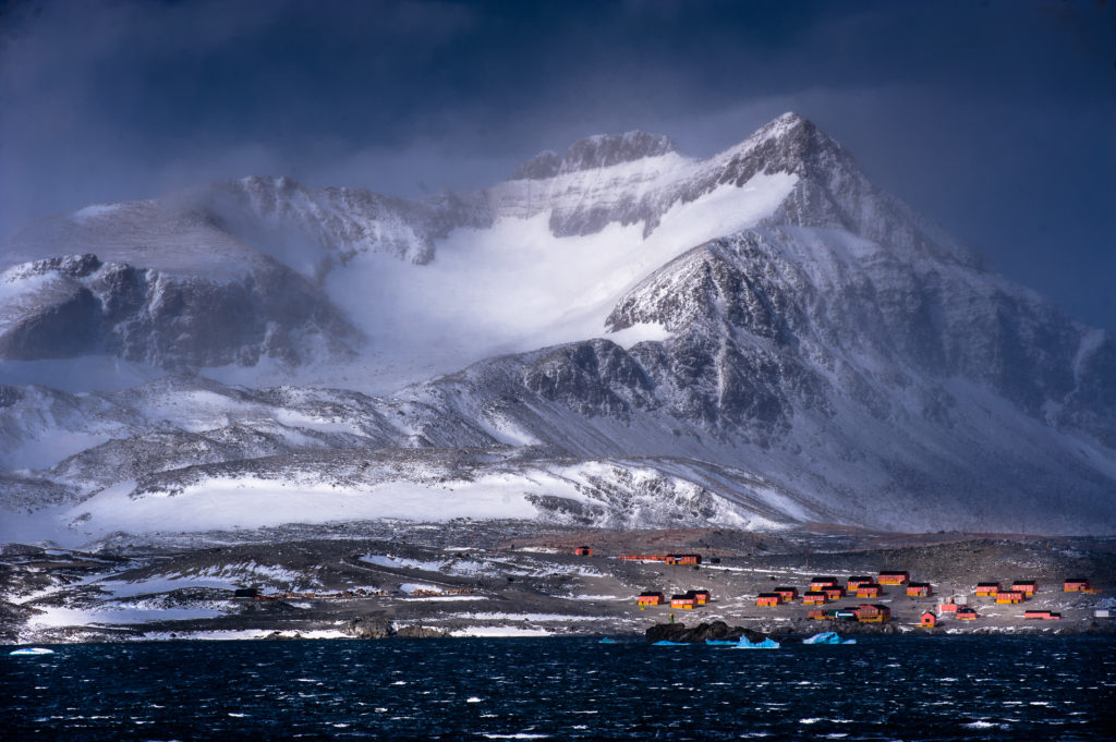 A stormy mountainous scene at the tip of the Antarctic peninsular. An Antarctic research base is seen at the foot of the mountain