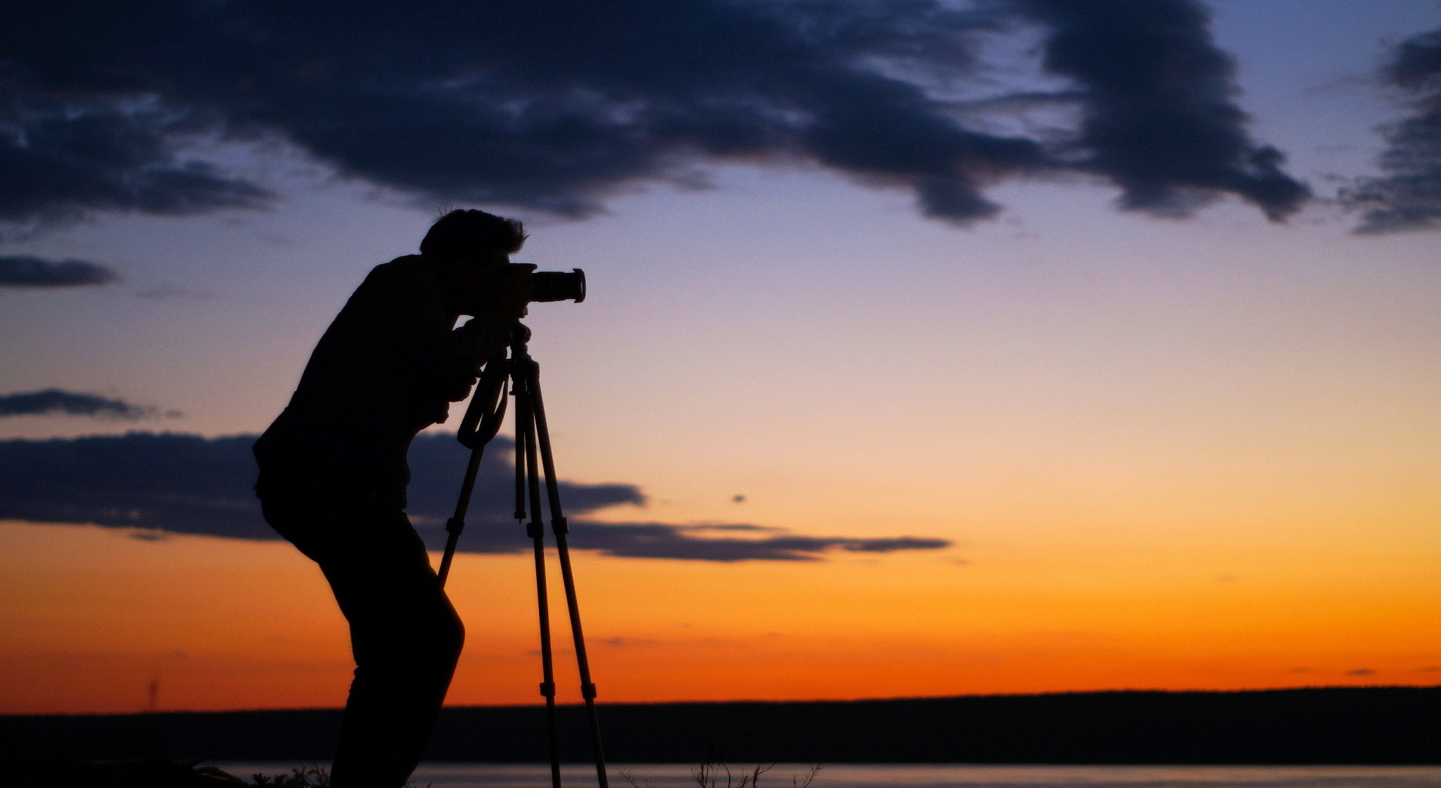 A photographer shooting from a tripod with a beautiful sunset behind