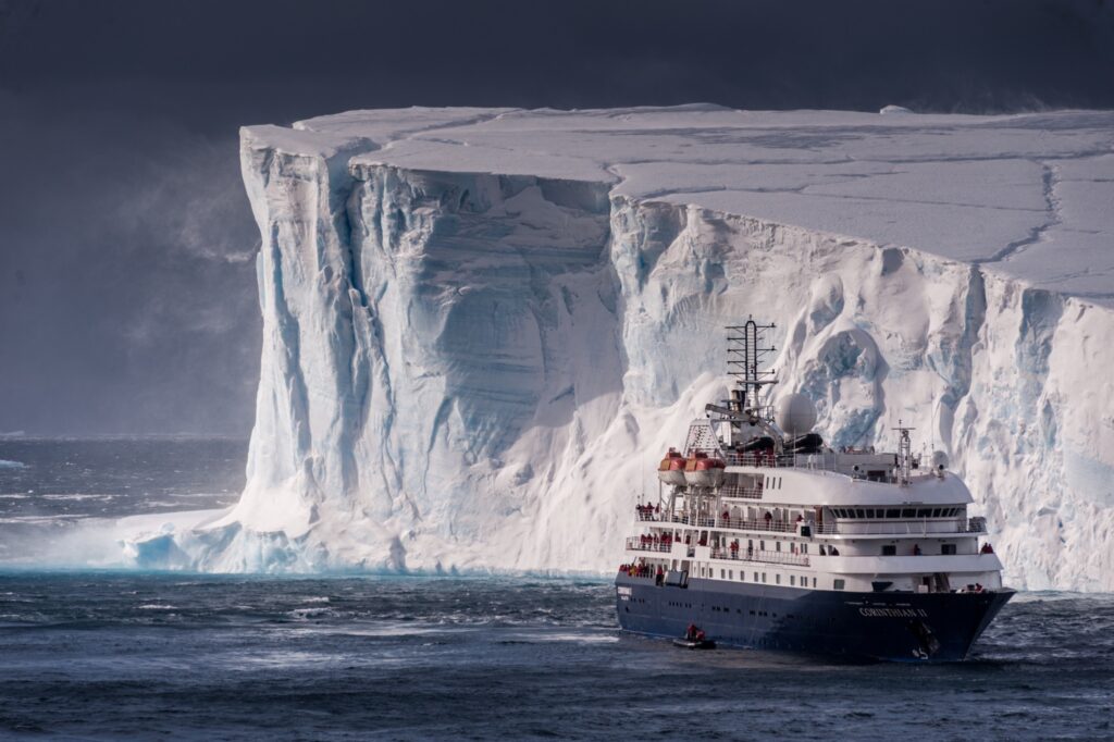 A small cruise ship in front of a large tabular iceberg in Antarctica