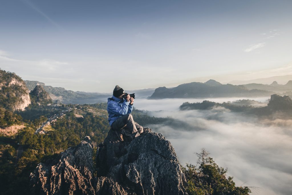 Man sitting atop a mountain taking a photograph