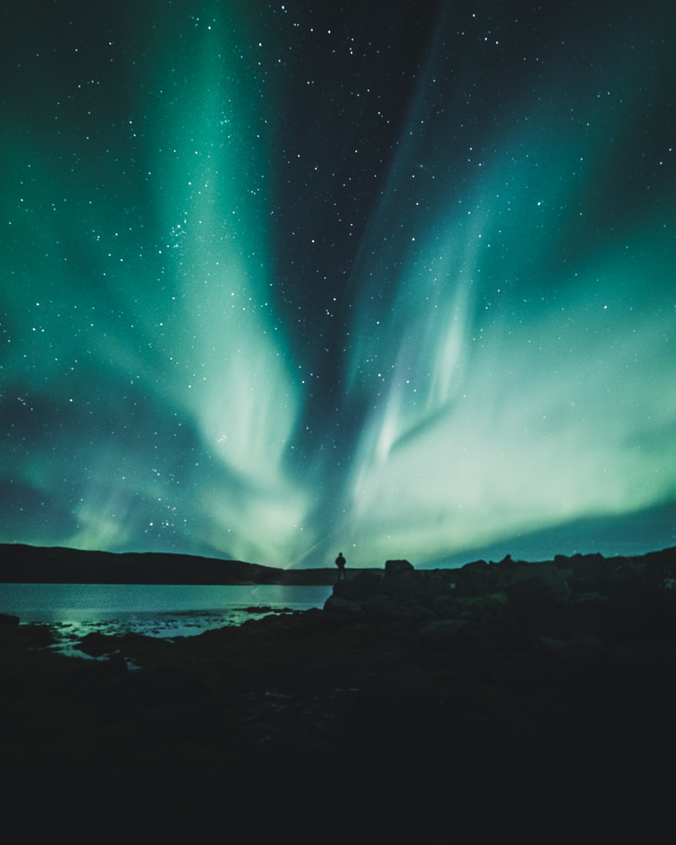 person standing near body of water during aurora northern sky