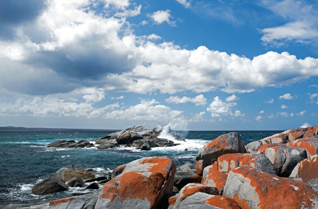 wave splashing on rock under white and blue sky