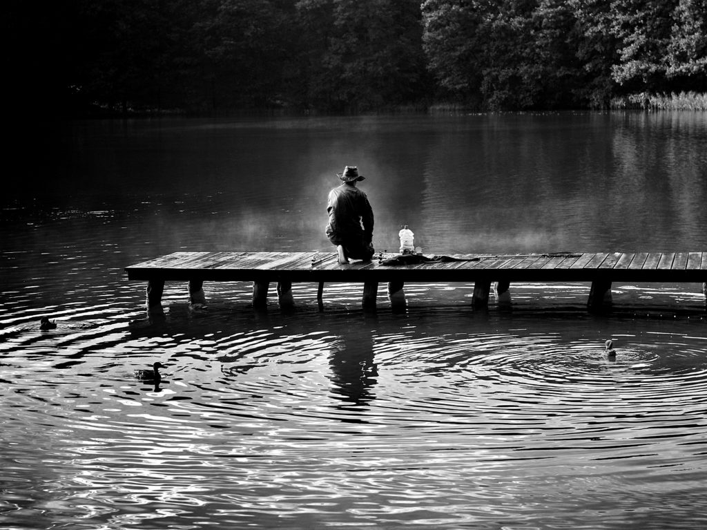 River with fisherman and jetty in black and white