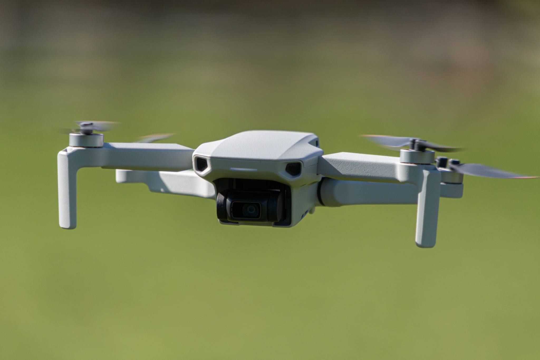 Close up of a DJI Mini drone in flight with a green out of focus background