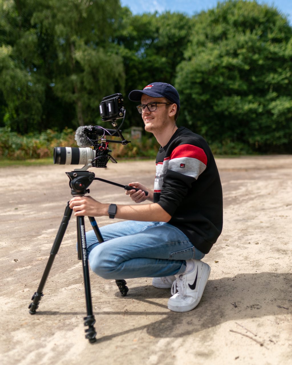 Man squats beside his camera and tripod