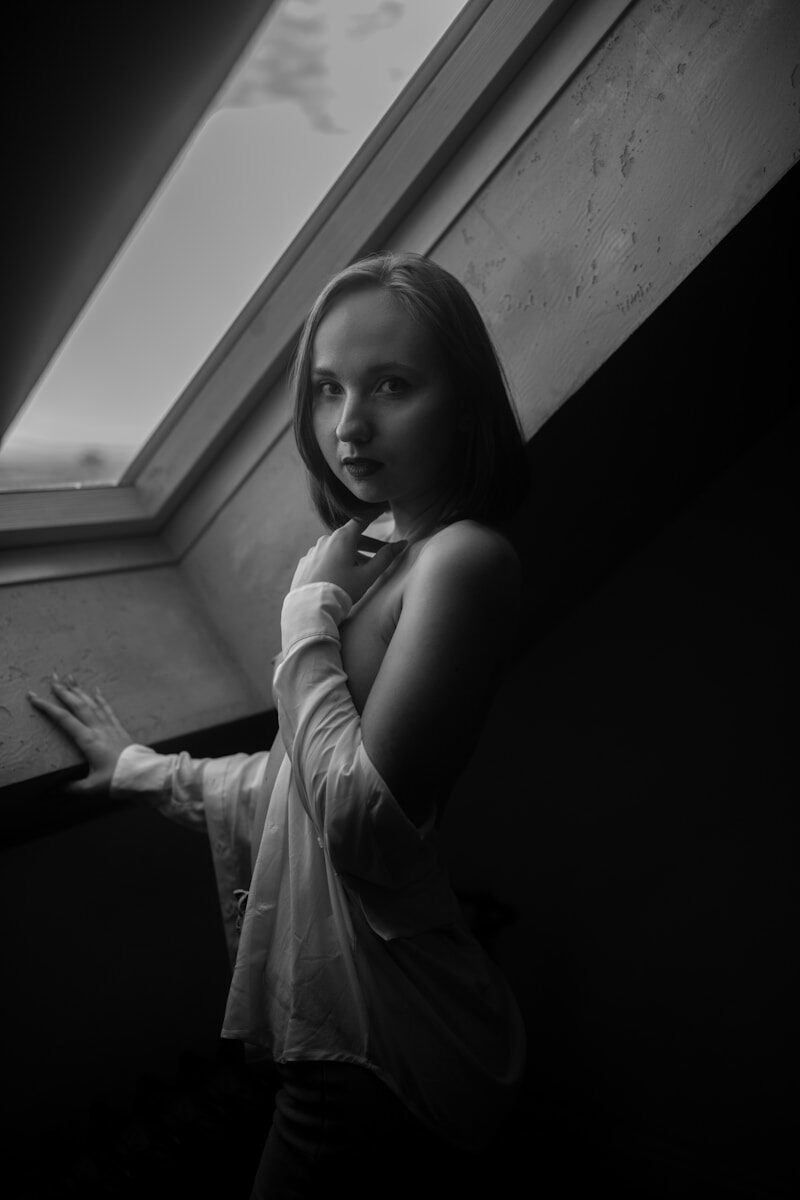 Young woman posing by a window in black and white.