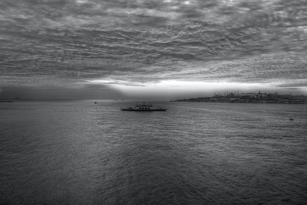 gray scale photo of a boat on body of water under cloudy sky