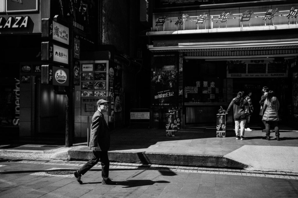 grayscale photo of man walking on sidewalk