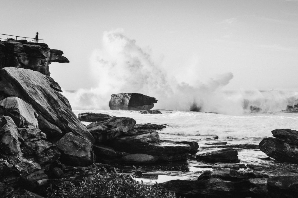 grayscale photo of manstanding at the edge of a cliff