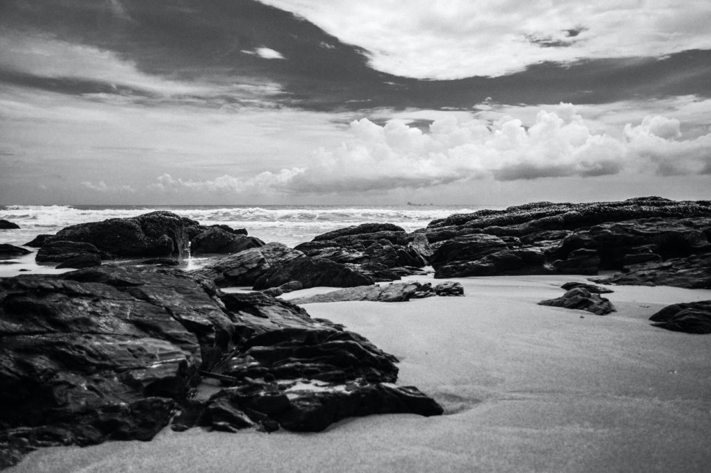 grayscale photography of rocks on seashore during daytime