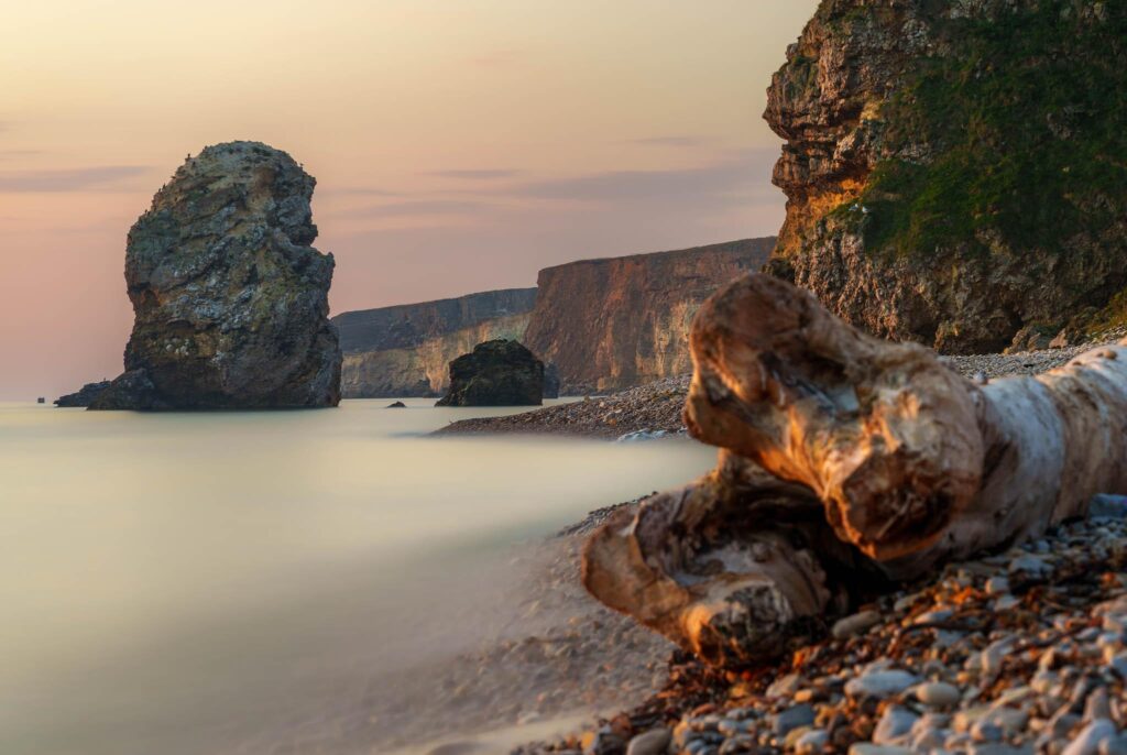 Long exposure of Marsden Beach in North East England with ethereal water and a golden sunrise