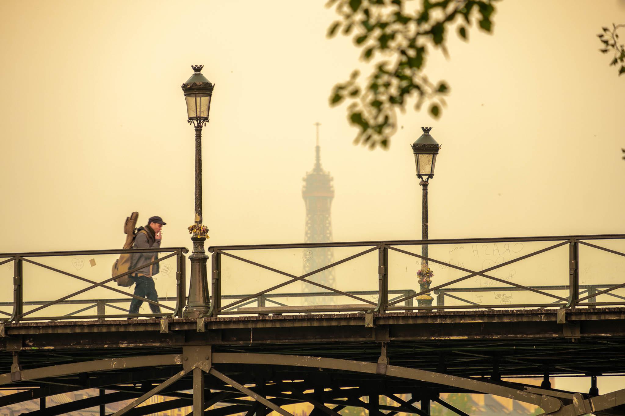 Man walking over bridge in Paris whilst smoking cigarette. Eiffel tower is in the background