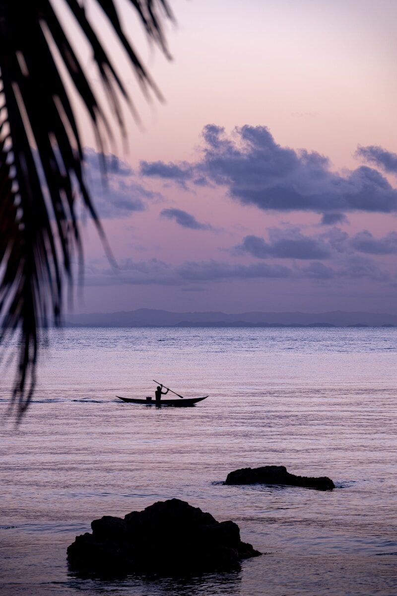 Silhouetted boatman on tranquil sea under a colorful twilight sky.