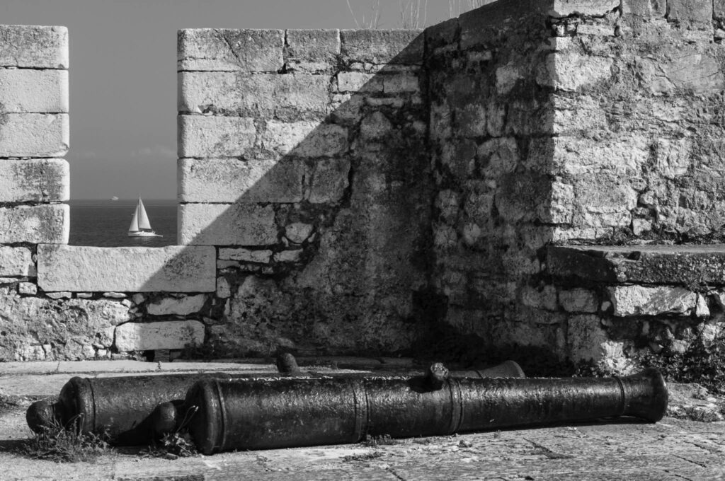 Old canon beside the walls of Corfu castle in Greece with yacht passing
