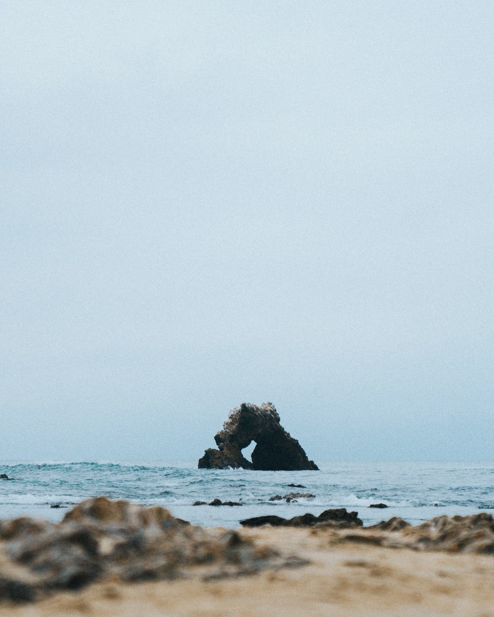 selective focus photography of rock monolith at the middle of the sea