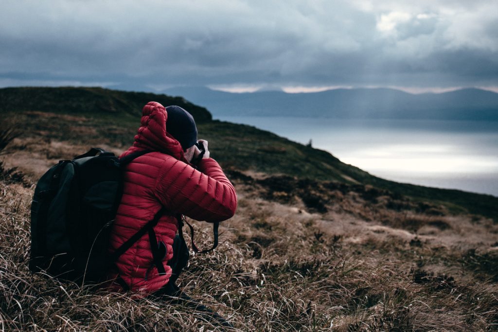 person in red hoodie taking a photo of wilderness