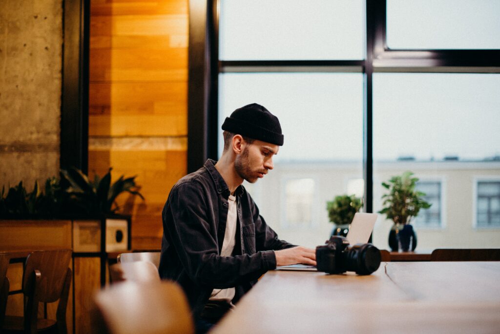 Man with camera and laptop sitting beside a window