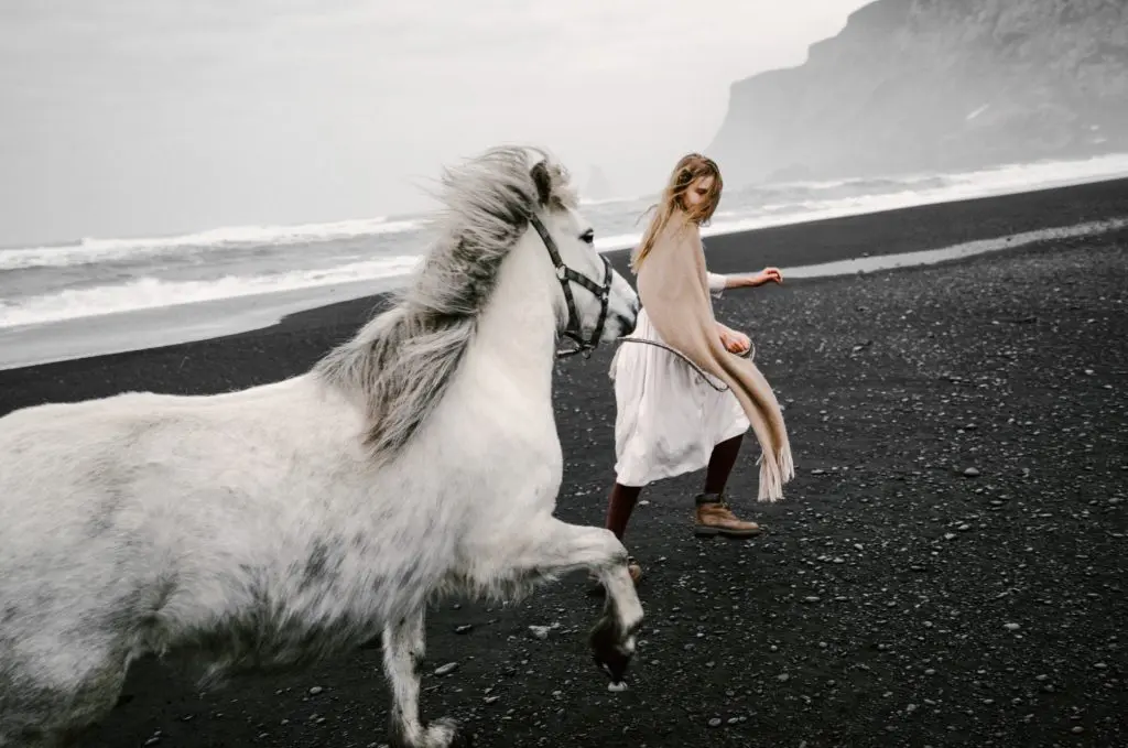 Young girl running on beach with beautiful white horse. Shot with Dutch Tilt. 