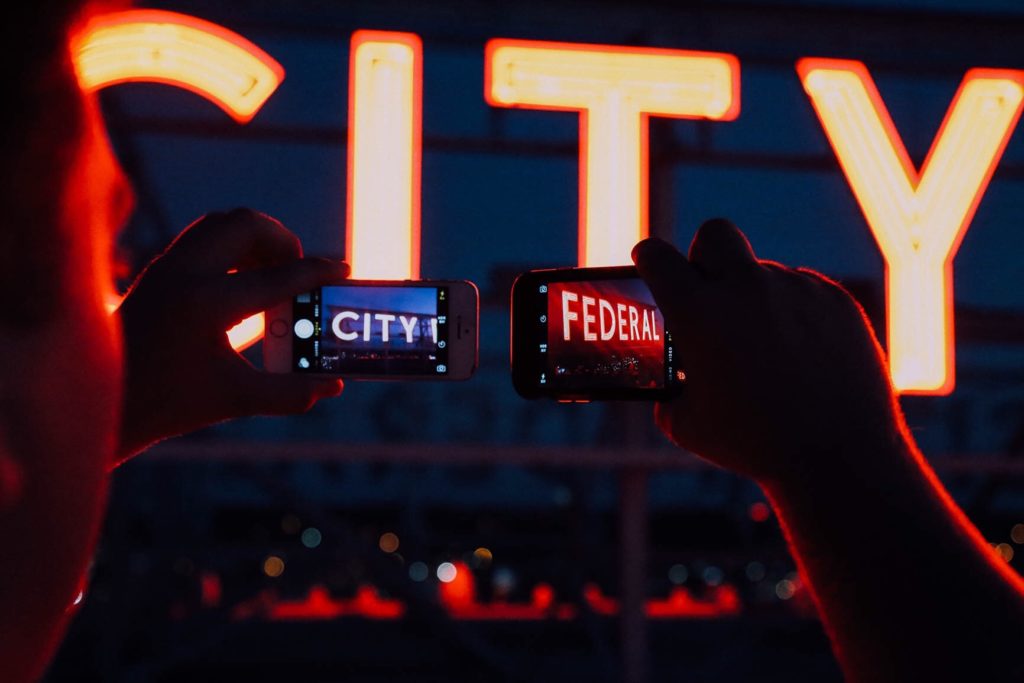 Man using two phones to take photo of neon sign