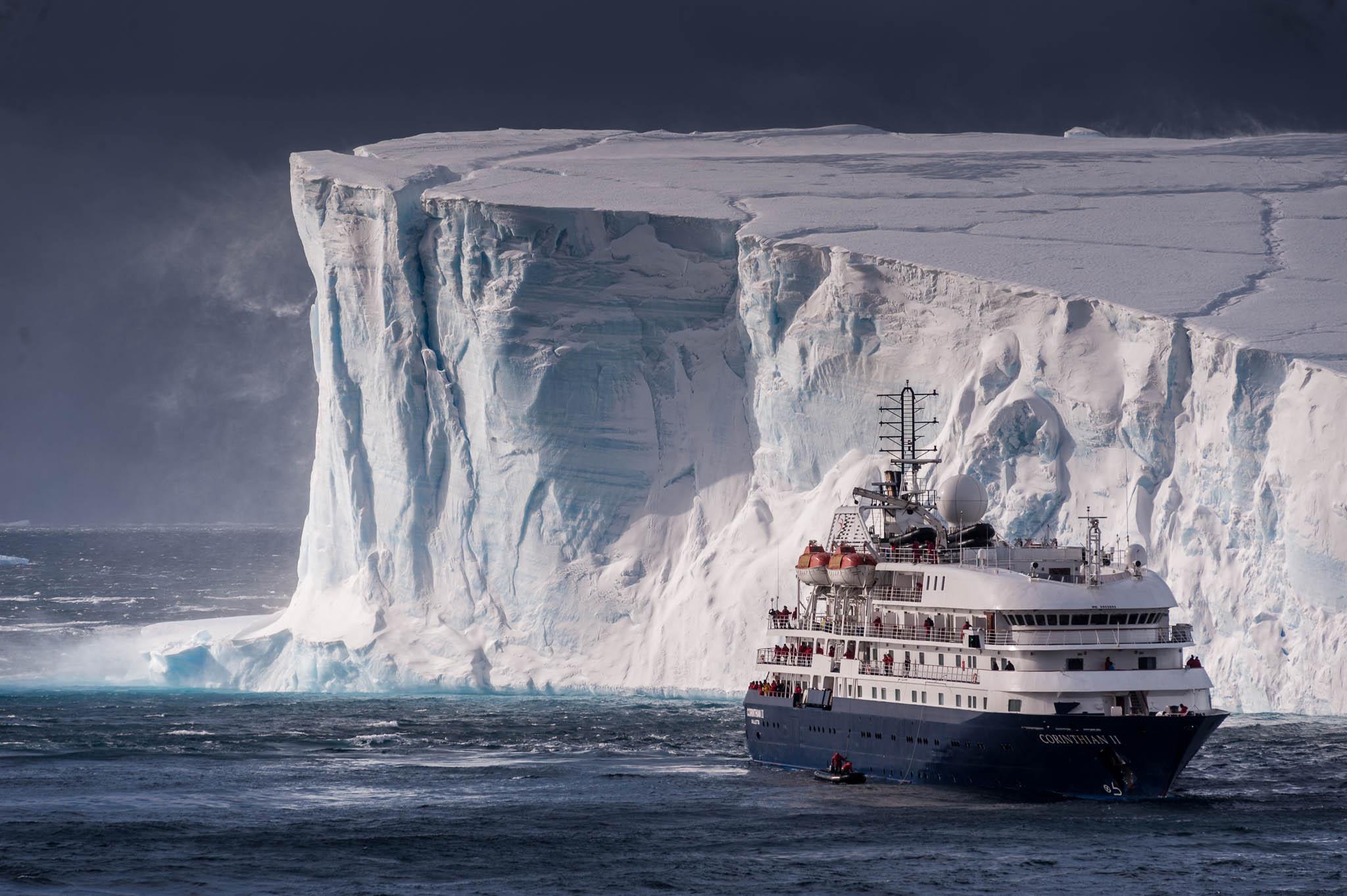 Small cruise ship in front of a large tabular iceberg in Antarctica