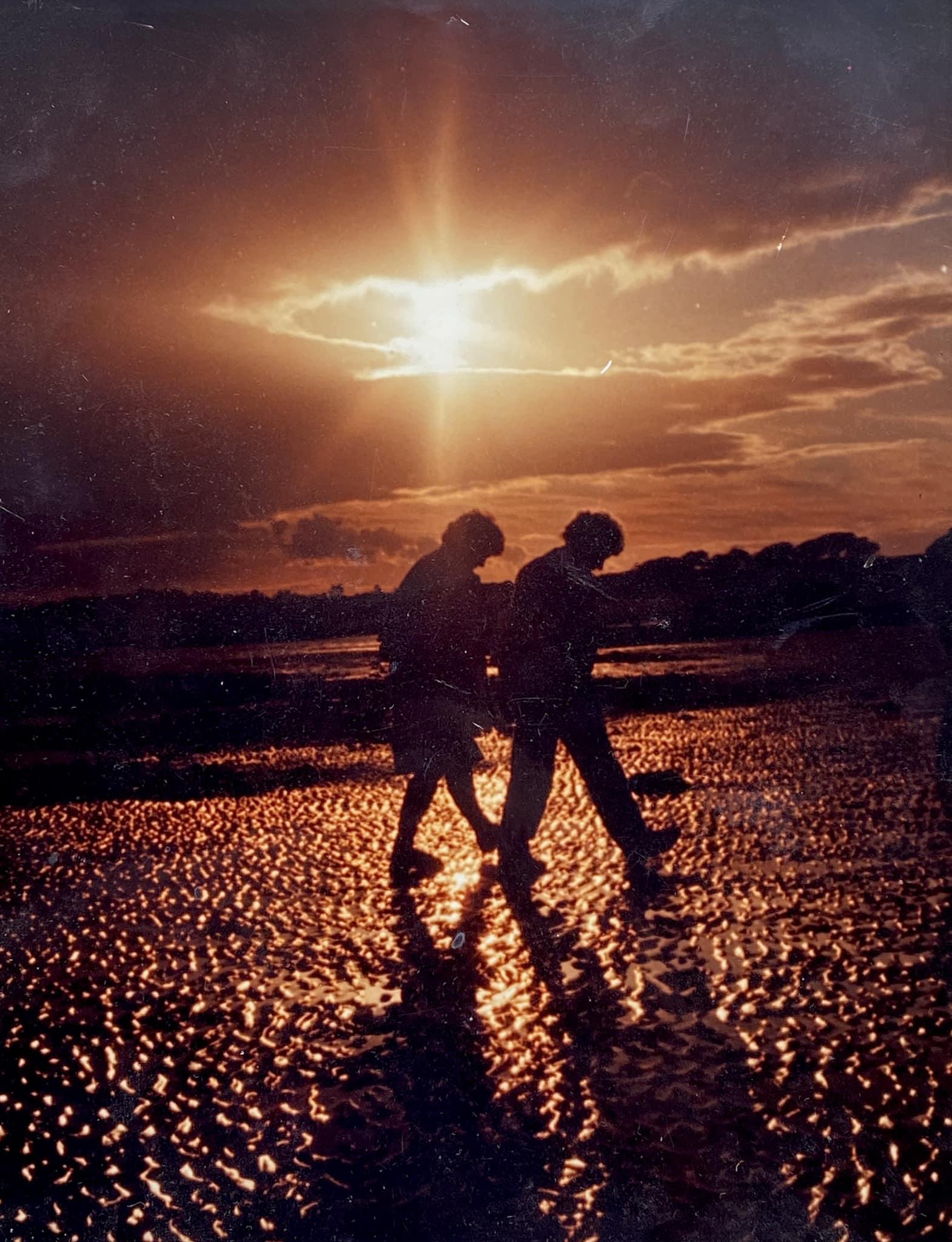 Two people walk up a beach at sunset. Shot on film in the 1980s