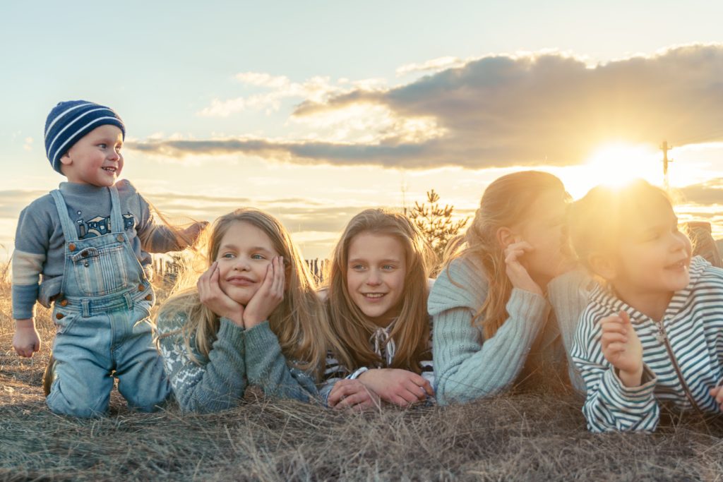 a group of children sitting on a field with the sun behind them
