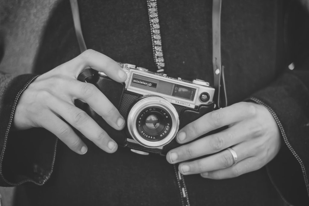grayscale photo of person holding fixed lens camera