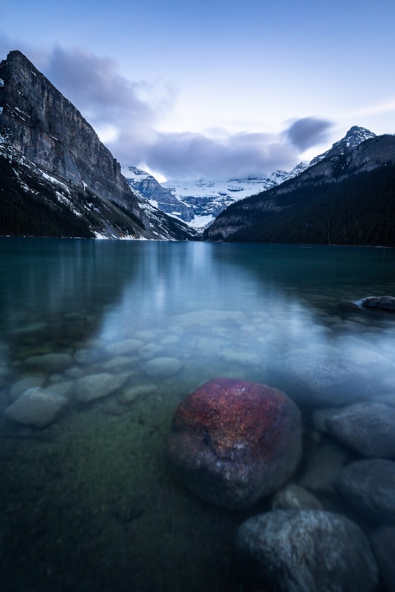 Clear mountain lake, snow-capped peaks, and a red rock.