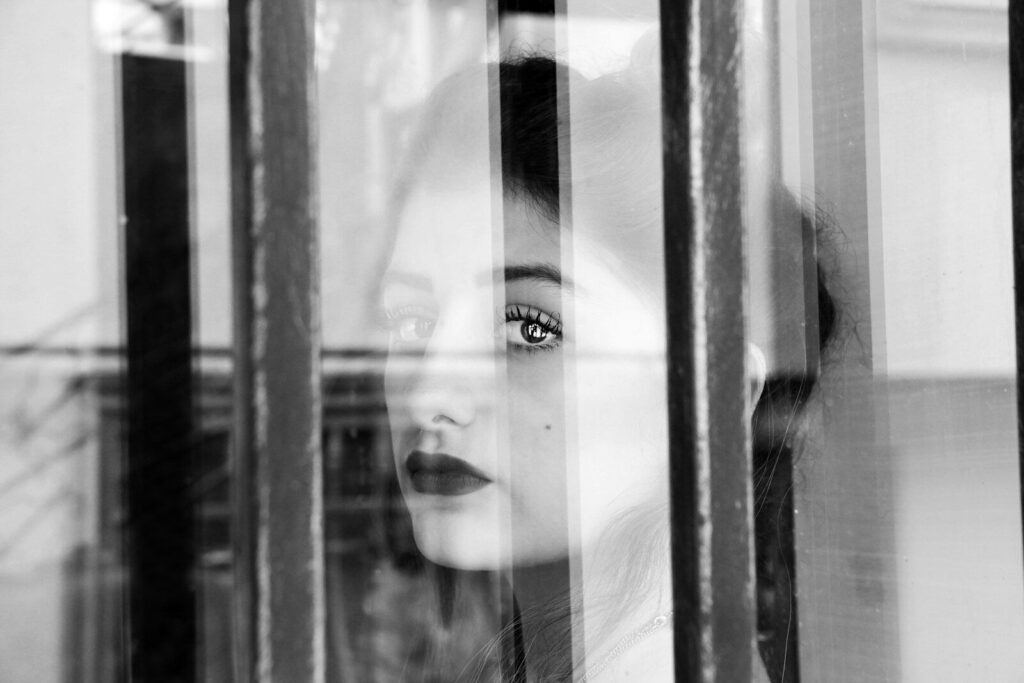 grayscale photography of woman beside glass window
