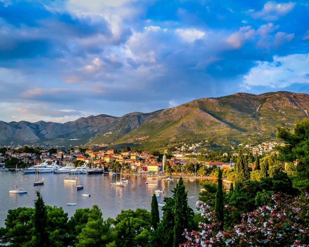 boats on body of water surrounded by trees and houses near mountain under blue and white sky at daytime